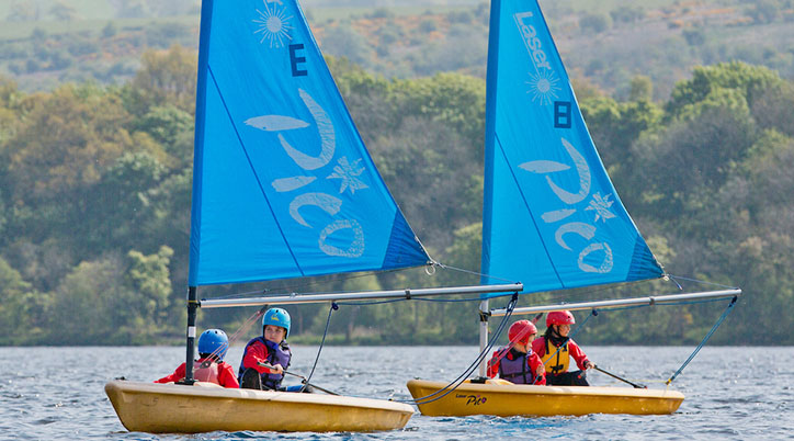 Four children on 2 boats on the water at Castle Semple Loch.